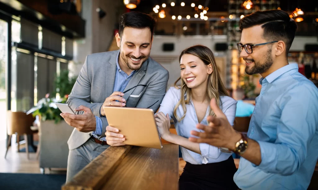 Three professionals reviewing lighting plans on a tablet in a modern hospitality setting, representing lighting consultants at work.