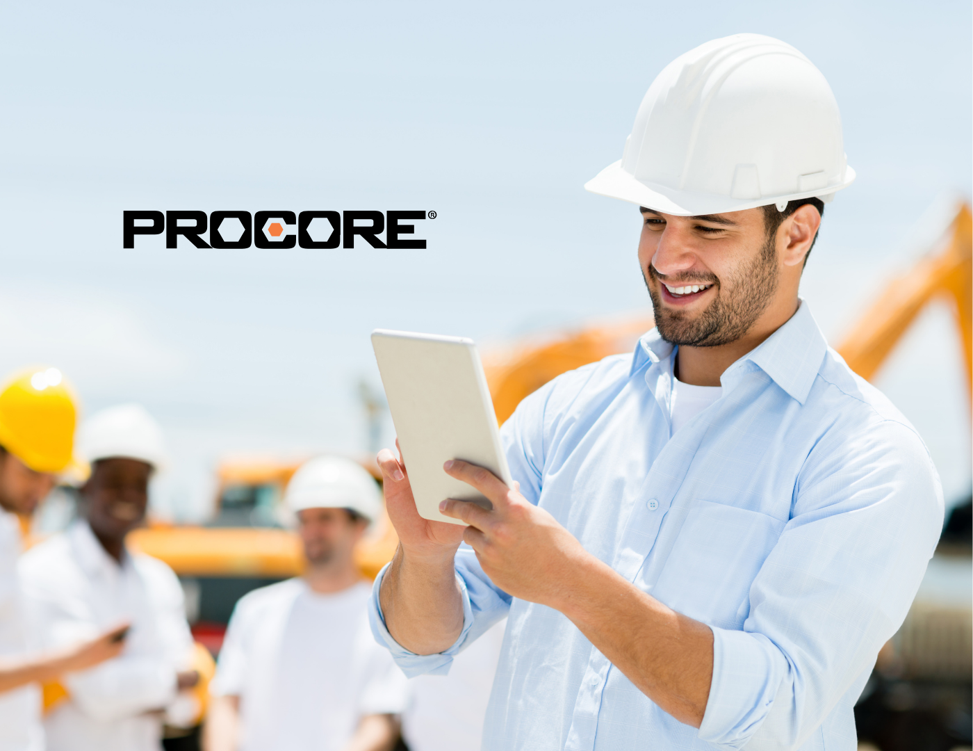 Construction manager using Procore software on-site via tablet, with team in background and heavy equipment visible.